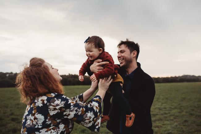 Mother reaching for daughter who is being held by father with Perth family photographer at Perry's Paddock