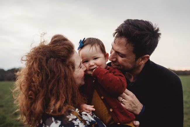 Parents smiling at daughter as they hold her with Perth family photographer at Perry's Paddock