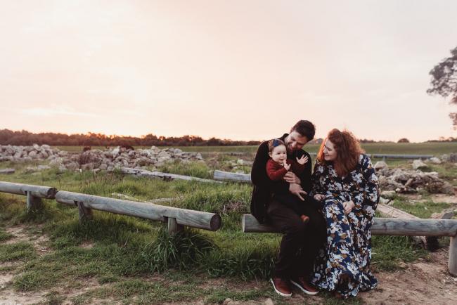 Parents sitting on a log with daughter who is clapping with Perth family photographer at Perry's Paddock