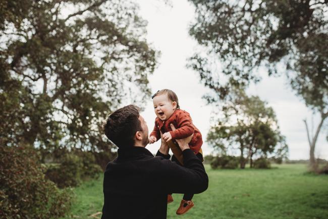 Father lifting baby daughter into the air who is laughing with Perth family photographer at Perry's Paddock