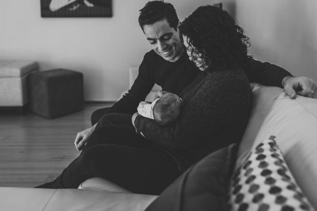 black and white image of mother and father sitting on the couch with their new baby with lifestyle newborn photographer Perth