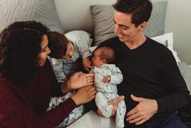 Father holding new baby as mother and brother touch him with lifestyle newborn photographer Perth