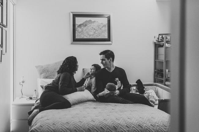 Black and white image of family of four on a bed with lifestyle newborn photographer Perth