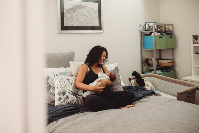 Mother laughing as she breastfeeds baby on her bed with lifestyle newborn photographer Perth