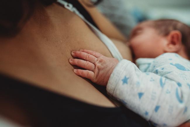 Close up of baby's hand on mother's chest as he breastfeeds with lifestyle newborn photographer Perth
