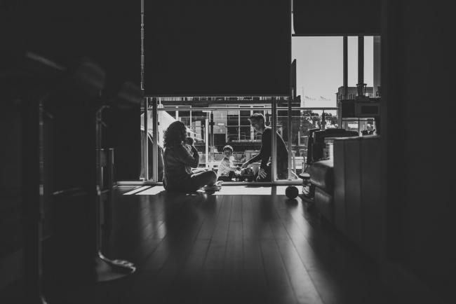 Black and white image of family of four on the floor in hard light with lifestyle newborn photographer Perth