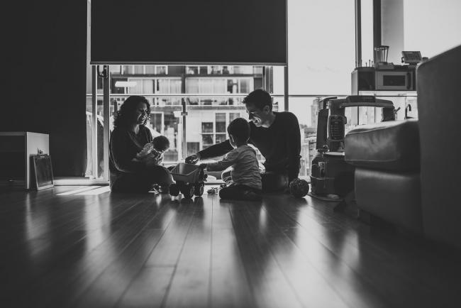 black and white image of family of four playing on the floor in hard light with lifestyle newborn photographer Perth