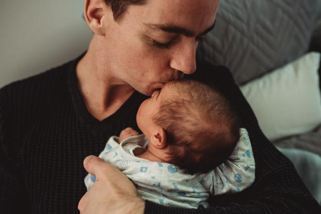 Father kissing baby's head with lifestyle newborn photographer Perth