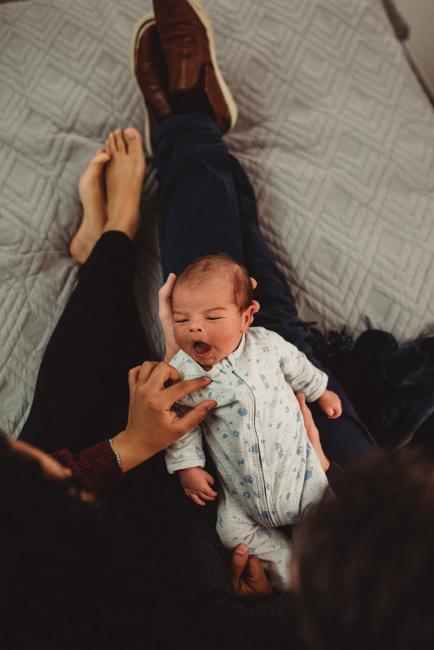 Baby laying across parents laps with lifestyle newborn photographer Perth