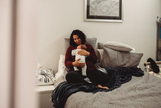 Mother holding baby on bed with lifestyle newborn photographer Perth