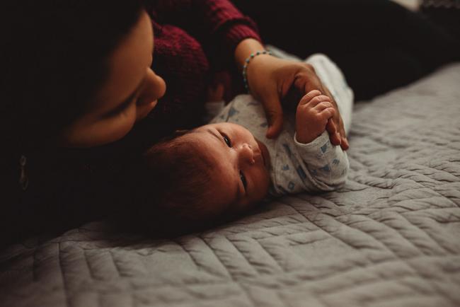 Mother laying on bed with baby with lifestyle newborn photographer Perth