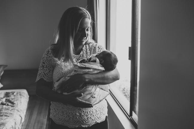 Perth-Newborn-Photographer-17-of-60 Black and white image of mother holding baby by a window with Perth newborn lifestyle photographer