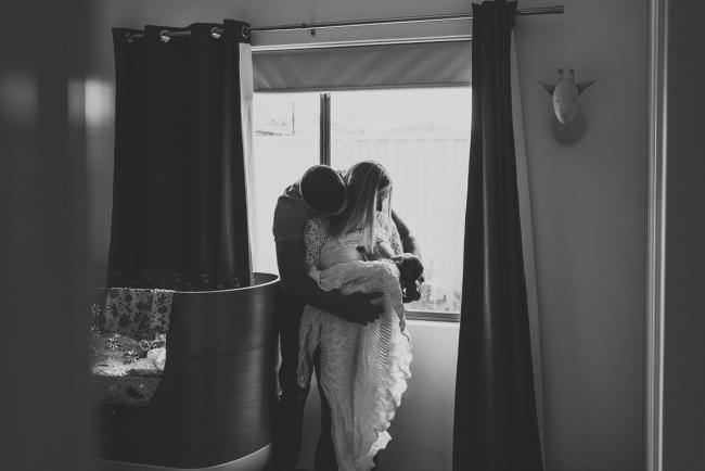 Black and white image of mother feeding new baby while father hugs them with Perth newborn lifestyle photographer