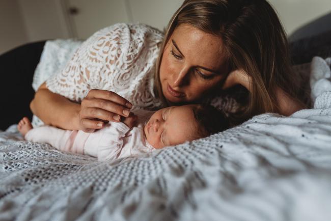 Perth-Newborn-Photographer-57-of-60 Mother laying next to newborn baby and holding her hand with Perth newborn lifestyle photographer