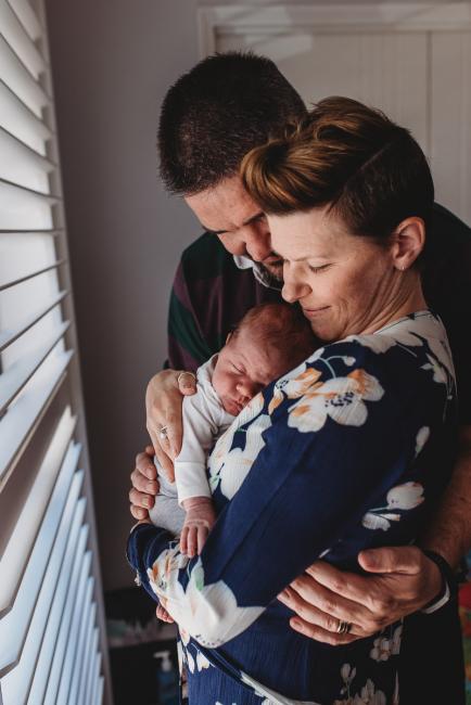 Parents hugging as mother holds sleeping newborn baby with Perth newborn lifestyle photographer