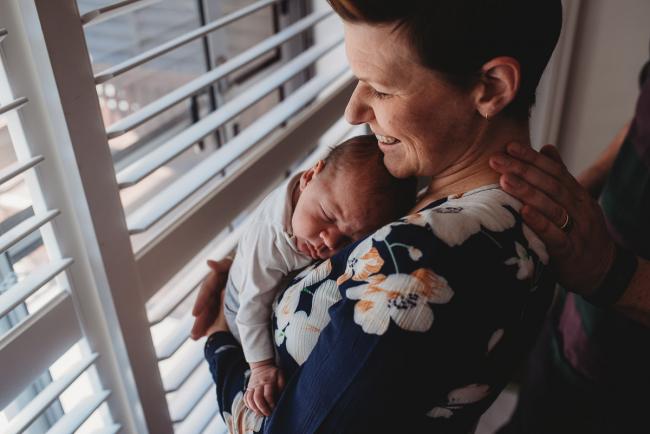 Mother holding newborn baby with husband's hand on her neck with Perth newborn lifestyle photographer