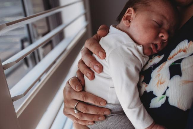 Parents hands on newborn baby back with Perth newborn lifestyle photographer