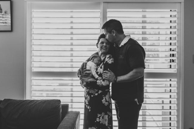 black and white image of parents holding newborn baby by a window with Perth newborn lifestyle photographer