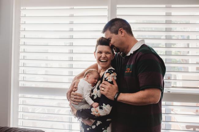 Parents holding newborn baby by window with Perth newborn lifestyle photographer