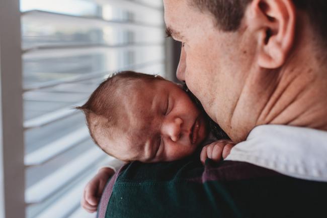 Father kissing newborn baby who is sleeping on his shoulder with Perth newborn lifestyle photographer