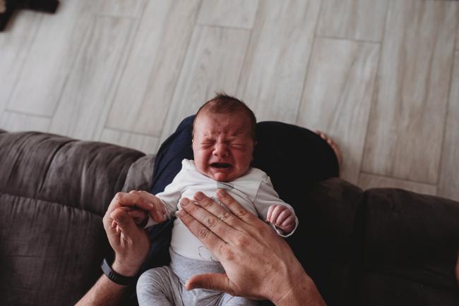 Newborn baby crying on father's lap with Perth newborn lifestyle photographer