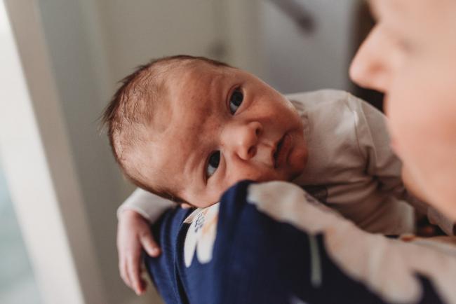 Newborn baby looking over shoulder of mother with Perth newborn lifestyle photographer