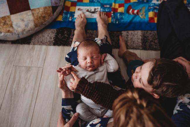 Baby across mother's lap as toddler touches his fingers with Perth newborn lifestyle photographer