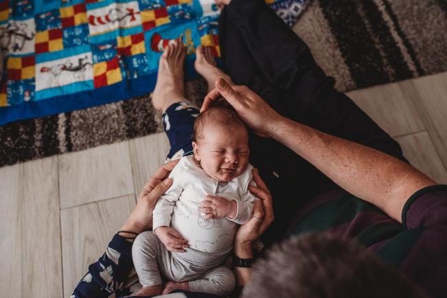 Newborn baby smiling as he lays across parents laps with Perth newborn lifestyle photographer