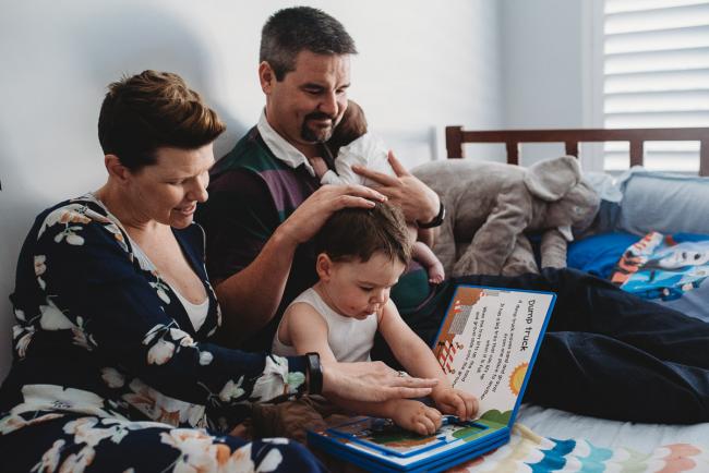 Parents reading on the bed with their toddler and newborn with Perth newborn lifestyle photographer