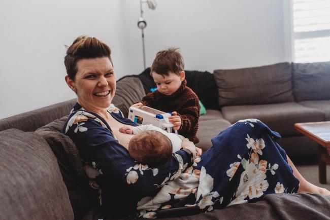 Mother feeding newborn baby on the couch while toddler plays with truck next to her with Perth newborn lifestyle photographer