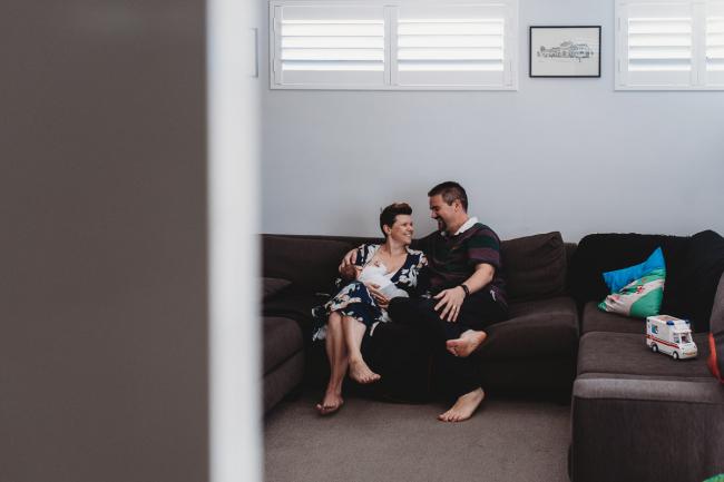 Parents on the couch with newborn baby with Perth newborn lifestyle photographer