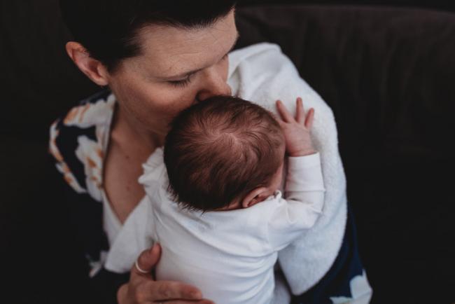 Mother kissing baby on her shoulder with Perth newborn lifestyle photographer