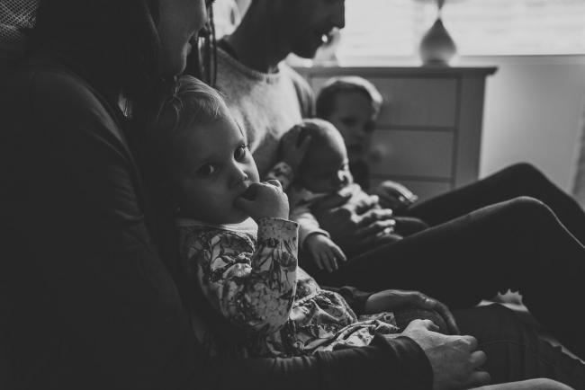 Black and white image of three kids on parents laps with lifestyle newborn photographer Perth