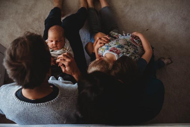 Top down image of three kids on parents laps with lifestyle newborn photographer Perth