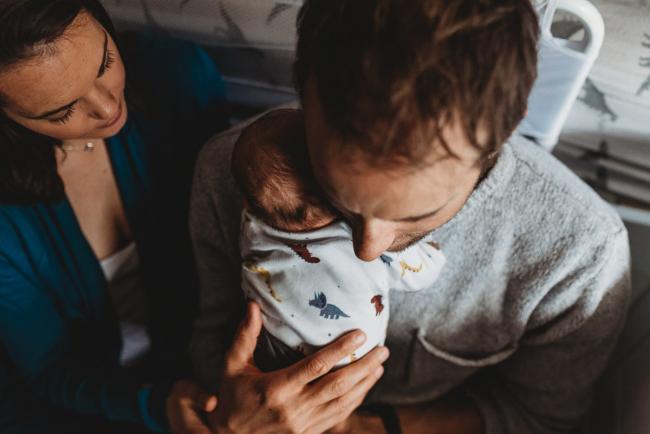 Father holding new baby on his shoulder with mother looking on with lifestyle newborn photographer Perth