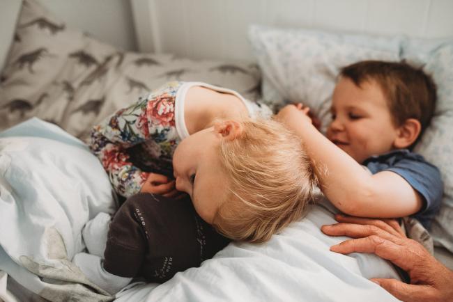 Three kids in bed with lifestyle newborn photographer Perth