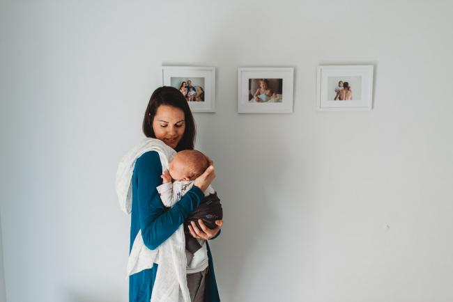 mother holding newborn baby against white wall with lifestyle newborn photographer Perth