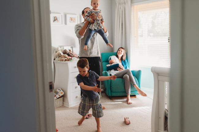 mother on chair with newborn baby while father lifts daughter in the air and little boy spins around with lifestyle newborn photographer Perth