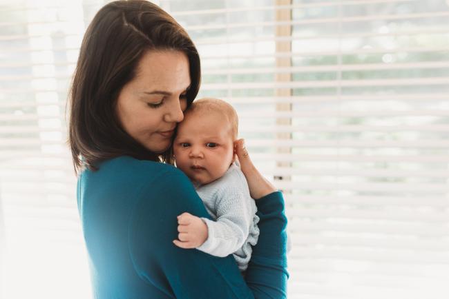 Mother holding newborn baby by window with lifestyle newborn photographer Perth