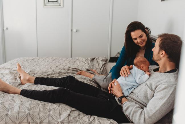Parents on bed with newborn baby with lifestyle newborn photographer Perth