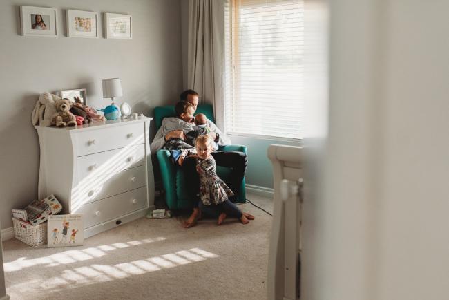 Father on chair in nursery with three kids with lifestyle newborn photographer Perth