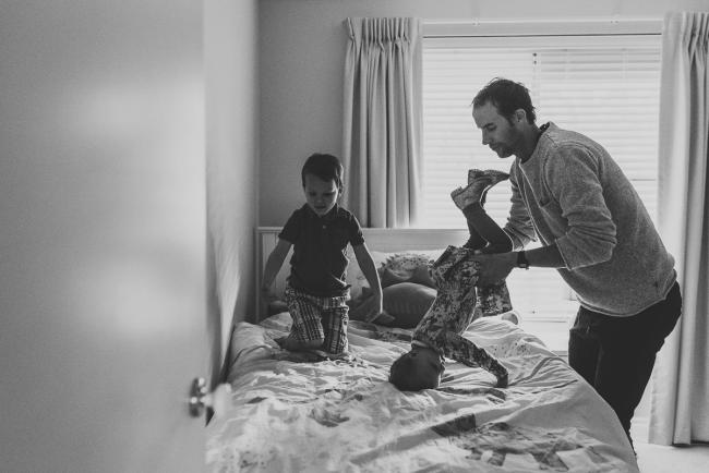 Black and white image of little boy jumping on bed and father tipping little girl upside down with lifestyle family photographer Perth