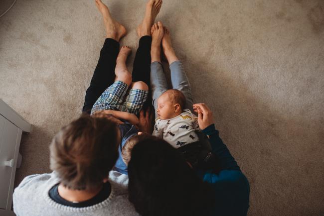 Top down image of parents with new baby and older son on their laps with lifestyle newborn photographer Perth