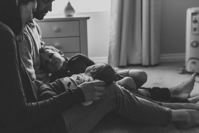 Black and white image of boys on parents laps with lifestyle newborn photographer Perth