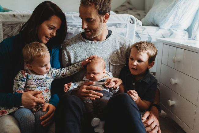 Parents sitting on the floor with their three children on their laps with lifestyle newborn photographer Perth