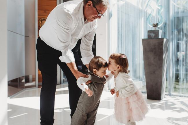 Little girl kissing little boy who is being held by his grandfather with Perth Events Photographer