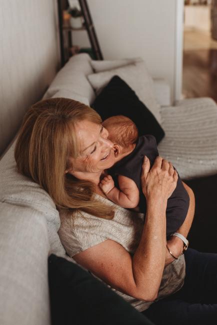 Lifestyle-Newborn-Photographer-Perth-18-of-69 Grandmother laughing as she holds newborn baby grandson on couch with in-home lifestyle newborn photographer Perth