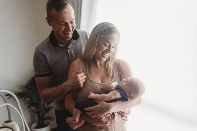 Parents smiling down at their newborn baby with in-home lifestyle newborn photographer Perth