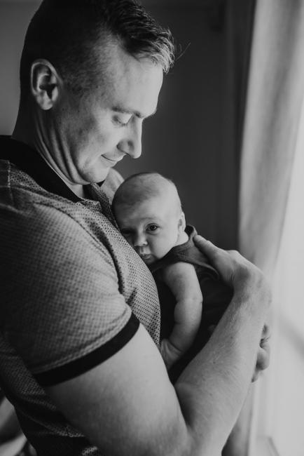 black and white image of newborn baby against father's chest with lifestyle newborn photographer Perth