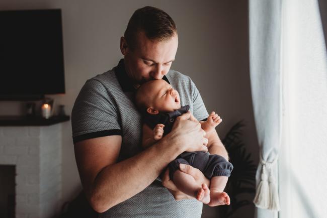 Father kissing newborn baby as the baby yawns with lifestyle newborn photographer Perth